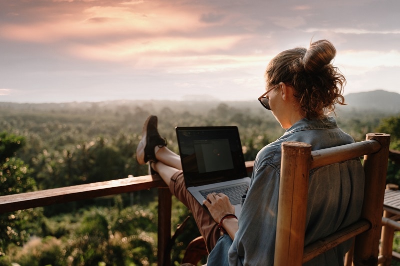 Girl wearing glasses sitting with laptop on deck that overlooks beautiful forest area